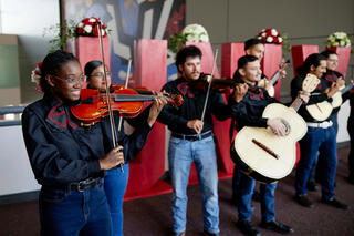 A group of students in a mariachi band play music in front of large red UNLV letters.